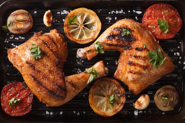 Two grilled chicken legs and vegetables on the grill pan close-up. horizontal view from above
