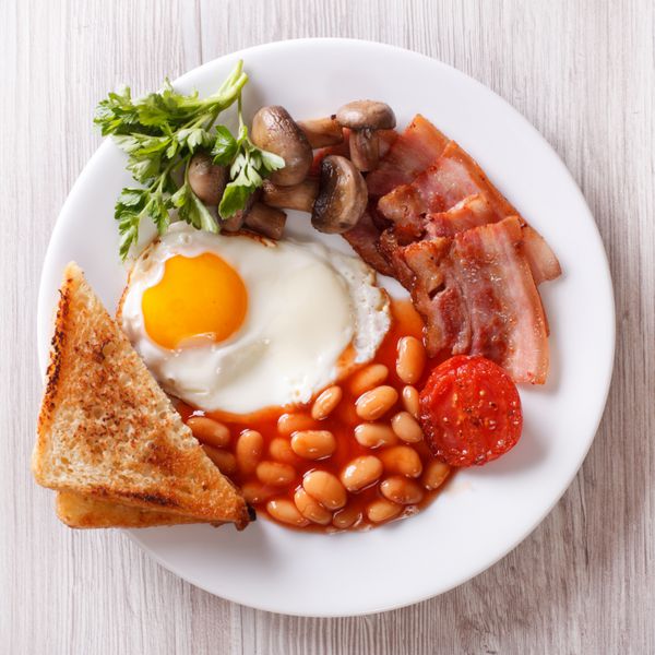 صبحانه انگلیسی تخم مرغ سرخ شده گوشت گاو لوبیا و نان تست بر روی یک صفحه نزدیک نمایش افقی از بالا