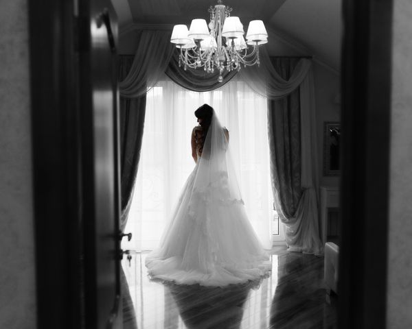 دختر عروس با موی بلند مواجهه با یک پنجره در لباس عروسی او