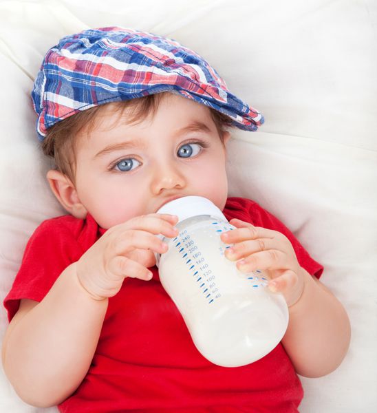 پرتره ناز کوچک گرسنه پسر بچه نوشیدن شیر دروغ گفتن بر روی بستر و خوردن غذا فرمول غذای کودک تغذیه سالم برای بچه ها