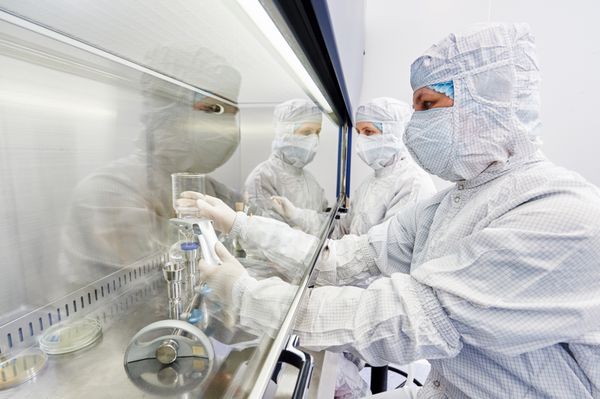 محققین علوم انسانی در لباس و تجهیزات حفاظتی با مواد خطرناک خطرناک در آزمایشگاه میکروبیولوژی کار می کنند