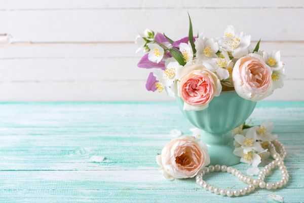 گل رز شیرین پاستل و گل یاس در گلدان بر روی زمینه ی چوبی فیروزه ای محل برای متن تمرکز انتخابی