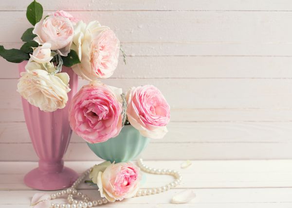 Sweet pink roses flowers in vases on white painted wooden background against white  wall. Selective focus. Place for text. Toned image.
