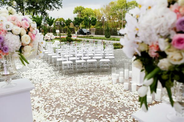 دسته گل های بزرگ از گل های سفید و بنفش بر روی ستون قبل از حیاط خیمه ای که برای مراسم عروسی آماده می شوند روی می دهد