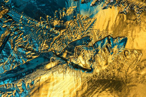 دنیای شگفت انگیز آب یخ زدگی یک نمای نزدیک و یا کلان یک یخ شکسته عکس گرفته شده در برابر پس زمینه آبی و طلایی