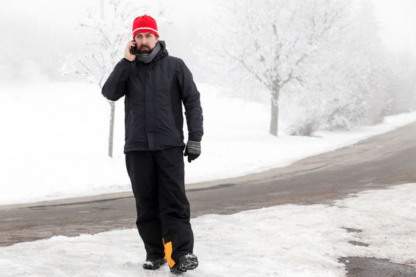 مرد با تلفن همراه در خیابان یخ زده راه می رود