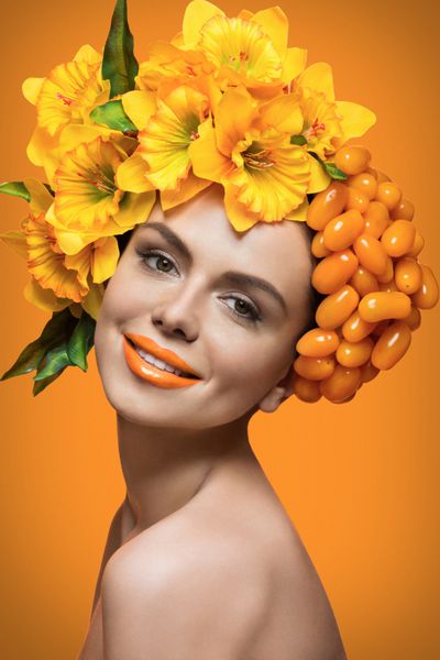 پرتره نزدیک از زن جوان زیبا با گوجه فرنگی گیلاس و نارسیوس گل در سر بیش از پس زمینه نارنجی