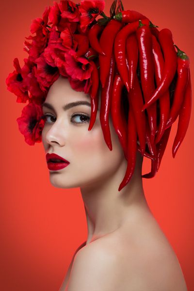 پرتره نزدیک از زن جوان زیبا با فلفل چوی و گل بر سر بیش از پس زمینه قرمز