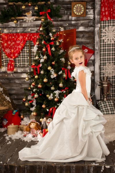 دختر ناز زیبا جوان لباس کریسمس و تیاردا را در موهای بلند خود می پوشد درخت کریسمس در پس زمینه وجود دارد