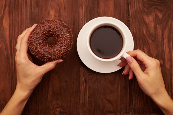 عکس زنانه را با شکلات دونات شکلات و فنجان قهوه روی میز چوبی قهوه ای بست