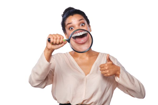 خنده دار زن لبخند زدن و نشان دادن دندان ها از طریق یک ذره بین حرکت دادن انگشت شست بالا در پس زمینه سفید