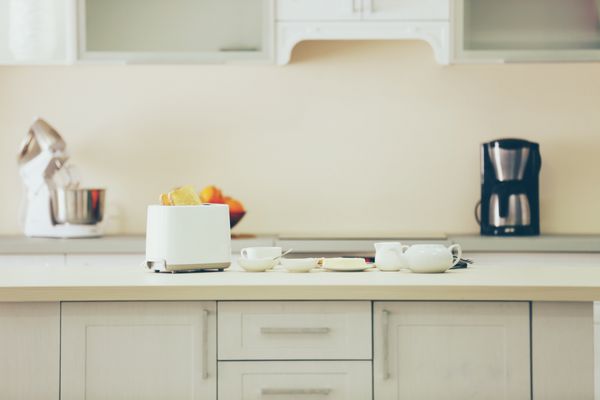 میز نازک چوبی با توستر و ظروف در یک زمینه آشپزخانه سفید