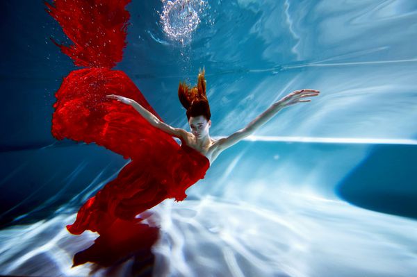 زیر آب در استخر با خالص آب دختر زیبا در یک لباس قرمز و موی سرخ