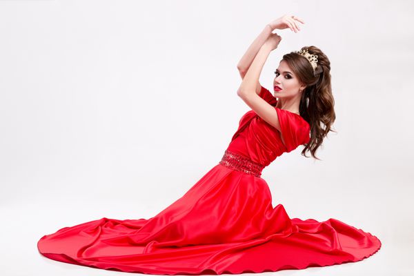زن زیبا در یک لباس قرمز طولانی روی زمین نشسته و دست ها را در بالا نگه می دارد