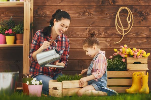 دختر بچه ناز کمک می کند تا مادر خود را برای مراقبت از گیاهان مادر و دخترش در حیاط خلوت باغبانی می کنند مفهوم بهار طبیعت و مراقبت