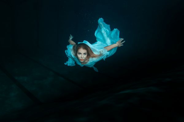 یک زن در یک لباس سفید به عنوان یک پری دریایی شنا در زیر آب