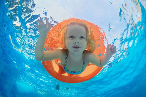 عکس های خنده دار زیر آب از دختر بچه شنا با سرگرم کننده در لوله پرتقال و غواصی در استخر آبی پارک آبی زندگی خانوادگی سالم و فعالیت ورزشی کودکان در کودکان با والدین در تعطیلات تابستانی