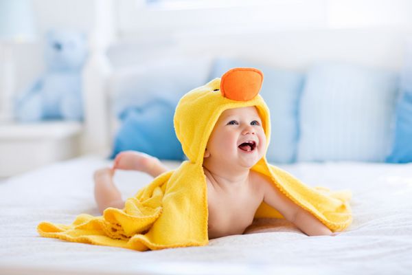 کودک خنده دار مبارک با استفاده از حوله اردک زرد با پوشش تخت نشسته روی تختخواب پدر و مادر بعد از حمام یا دوش کودک خشک را در اتاق خواب تمیز کنید حمام کردن و شستن بچه های کوچک بهداشت کودکان نساجی برای نوزادان