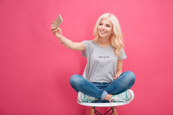 لبخند زدن زن جوان ساخت عکس selfie در گوشی های هوشمند پس زمینه صورتی