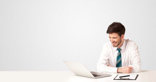 مرد کسب و کار در جدول سفید با لپ تاپ سفید در پس زمینه سفید نشسته است