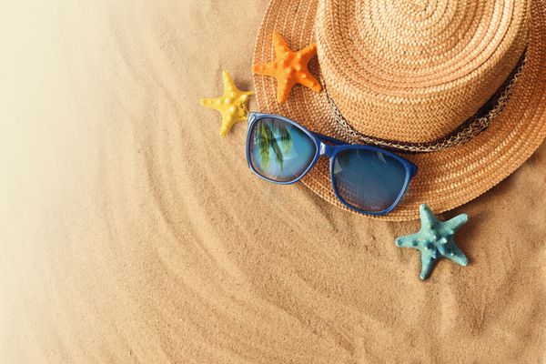 مفهوم تعطیلات تابستانی با کلاه نی و عینک آفتابی در ساحل شنی