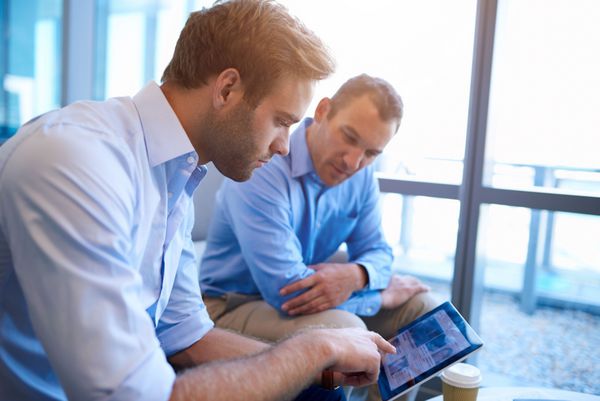 دو مدیر اجرایی نشسته در یک فضای دفتر روشن به دنبال اطلاعات با هم با به اشتراک گذاشتن صفحه نمایش یک قرص دیجیتال