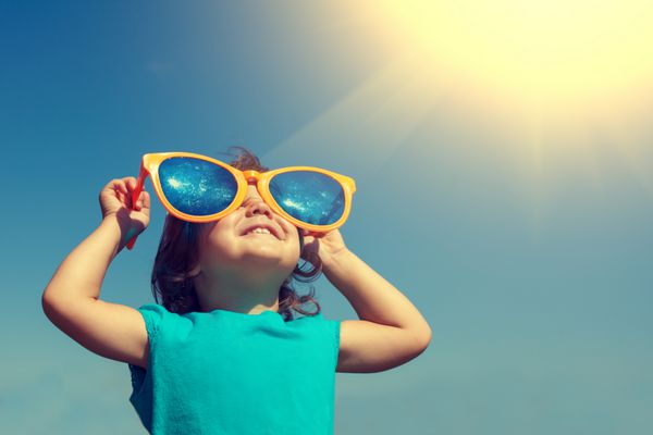 دختر کوچک مبارک با عینک آفتابی بزرگ به دنبال خورشید است