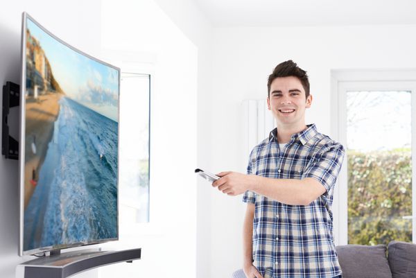 مرد جوان با تلویزیون صفحه نمایش منحنی جدید در خانه