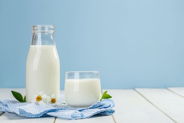 یک بطری شیر و شکر شیر بر روی یک میز چوبی سفید روی پس زمینه آبی محصولات لبنی خوشمزه مغذی و سالم
