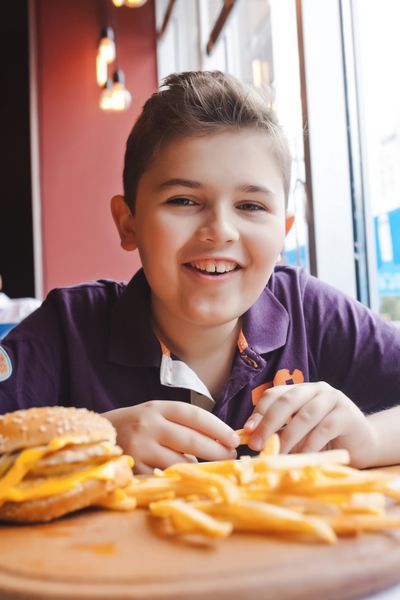 پسر کوچک خنده دار یک همبرگر در یک کافه مفهوم غذا خوردن