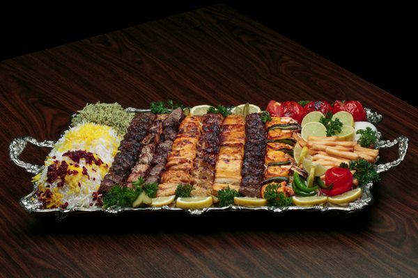 نمایش کامل مخلوط کباب ایرانی از گوشت چرخ کرده و مرغ با برنج و سیب زمینی سرخ کرده و سبزیجات فرانسوی در یک سینی بزرگ سنتی روی میز چوبی