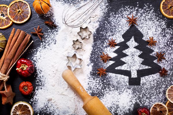 پخت و پز کریسمس صنوبر ساخته شده از آرد در یک جدول تاریک مواد تشکیل دهنده برای پخت و میوه های خشک شده در پس زمینه تاریک نمایش بالا