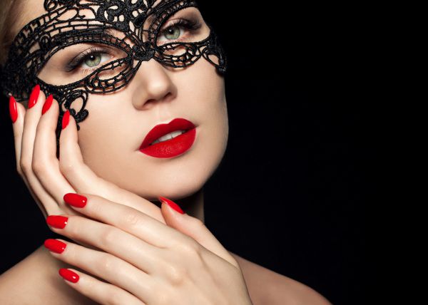زن زیبا با ماسک توری سیاه روی چشم او نزدیک لب لب و ناخن قرمز دهان باز مانیکور و آرایش مفهوم را تشکیل دهید شور جدا شده بر روی زمینه سیاه و سفید