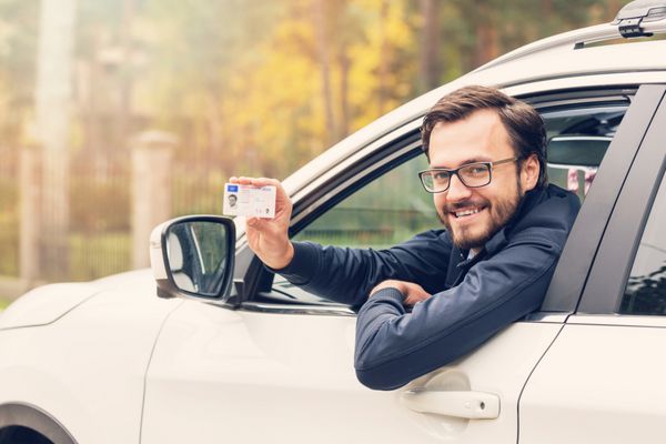 مرد نشسته در ماشین و مجوز رانندگی خود را نشان می دهد