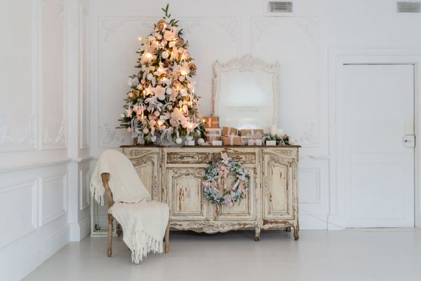 درخت کریسمس در صندلی چوبی کمد دفتر کمدی در داخلی سفید تزئین شده با گل مصنوعی گل سرخ و اسباب بازی