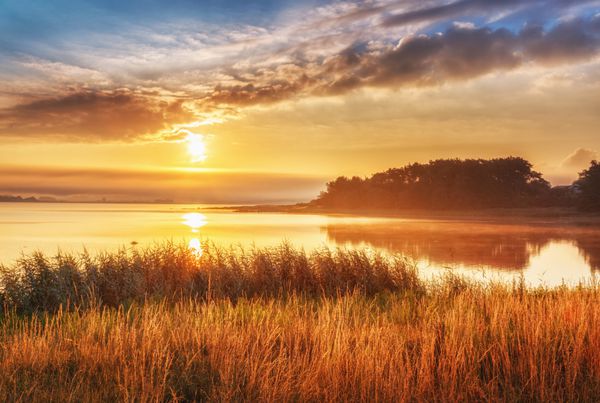 چشم انداز طلوع خورشید زیبا در دریای شمال سوئد مناظر حماسی با چمن های بالایی در پیشانی و دریا در حال افزایش در خورشید صبح و آسمان درخشان و ابرها در پس زمینه