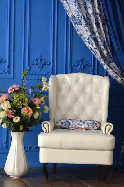 صندلی سفید یک گلدان گل در اتاق با دیوارهای آبی