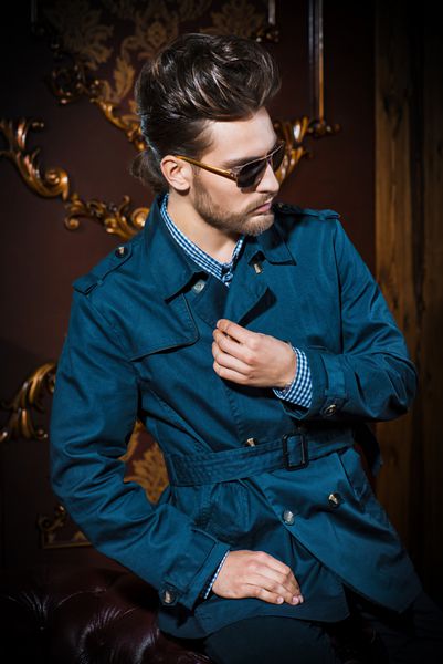 Portrait of a well-dressed imposing man in sunglasses standing in apartments with luxurious classic interior Men