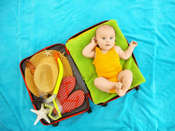 کودک ناز و چیزهایی برای تعطیلات در چمدان دروغ گفتن روی روکش آبی تعطیلات در دریا با کودک مفهوم
