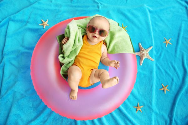 کودک ناز با حلقه شنا حوله و عینک آفتابی که روی تخت آبی قرار دارد تعطیلات در دریا با کودک مفهوم
