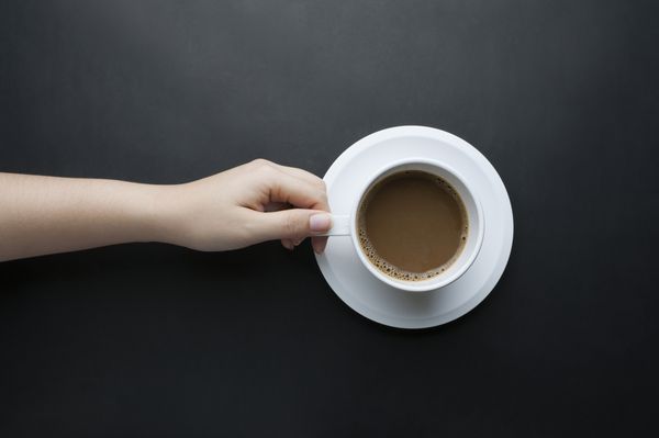 دست در دست داشتن یک فنجان سفید قهوه در پس زمینه سیاه و سفید