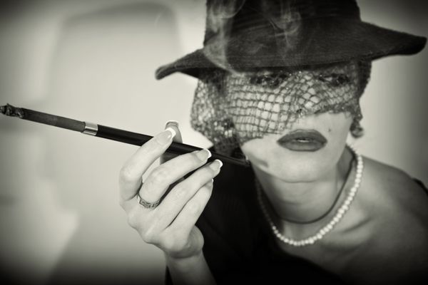 زن زیبا جوان با سیگار در دهان در کلاه با حجاب