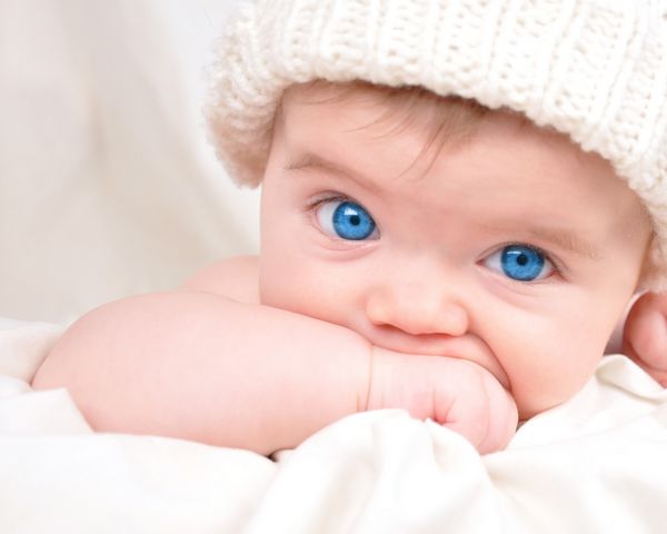 یک کودک جوان به دوربین نگاه می کند و دست خود را مکیدن می دهد کودک پوشیدن کلاه و چشم های آبی روشن دارد از آن برای یک مفهوم والدین یا عشق استفاده کنید