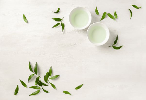 مفهوم چای دو فنجان سفید چای که با برگ چای سبز محصور شده است از بالا به نظر می رسد فضای متن