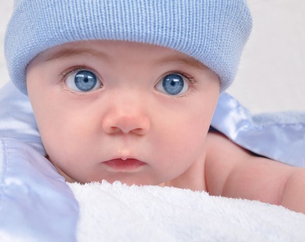 یک بچه کوچک با چشم آبی با یک کلاه خیره شده است کودک روی پتو است