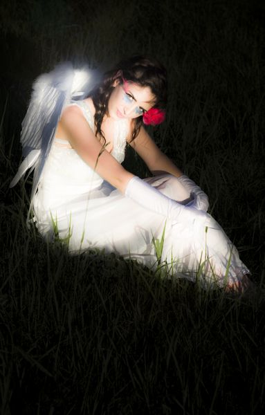 فرشته جادویی و درخشان فرشته مهاجم استراحت در یک چمنزار علفی در شب با بال خود را روشن صحنه تاریک در یک مفهوم فوقالعاده و عرفانی