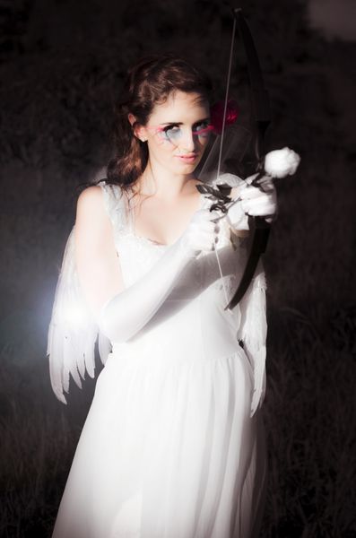 کوپید زیبایی الهه زیبایی ایستاده در همه لباس های سفید با بال در حالی که برگزاری یک کمان و گل رز آرایش آماده برای تنظیم نور عشق عشق