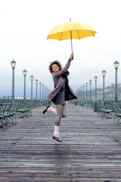 دختر زیبا آفریقایی آمریکایی با چتر زرد روی اسکله