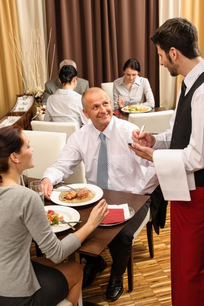 افراد کسب و کار توسط خدمتکار خدمت می کنند لذت بردن از ناهار در رستوران