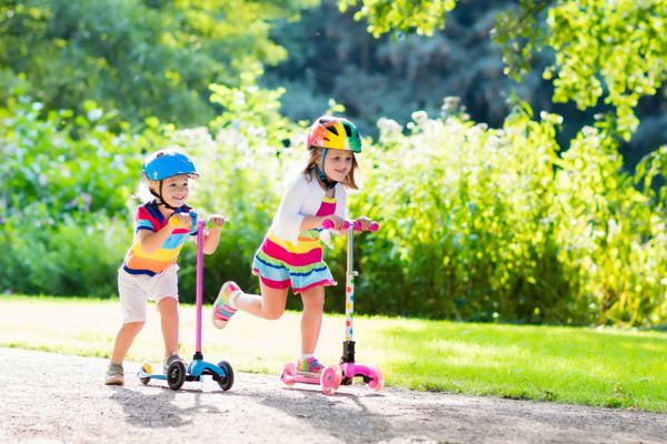 کودکان یاد می گیرند روروک مخصوص بچه ها در یک پارک در روز تابستان آفتابی سوار شوند پسر پیش دبستانی و دختر در کلاه ایمنی سوار غلتک کودکان در خارج از منزل با اسکوتر ها بازی می کنند اوقات فراغت فعال و ورزش در فضای باز برای کودک